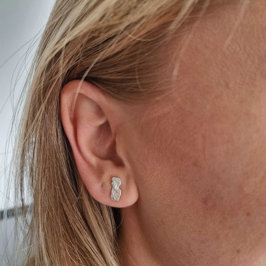 Close-up of an ear wearing a silver earring with blonde hair.