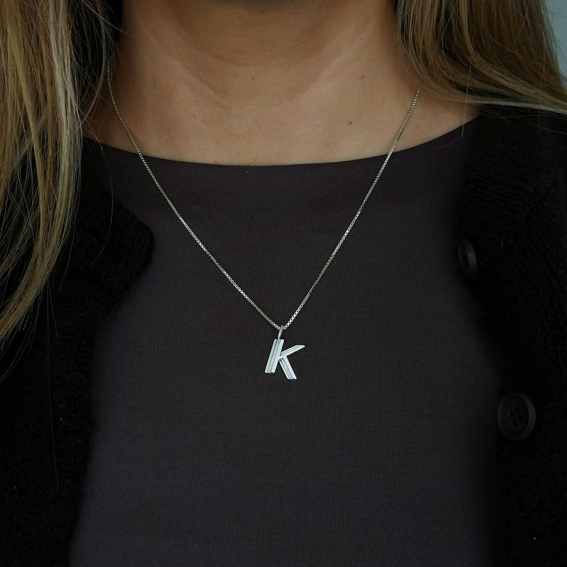 Silver necklace with a 'K' pendant worn by a person against a dark background