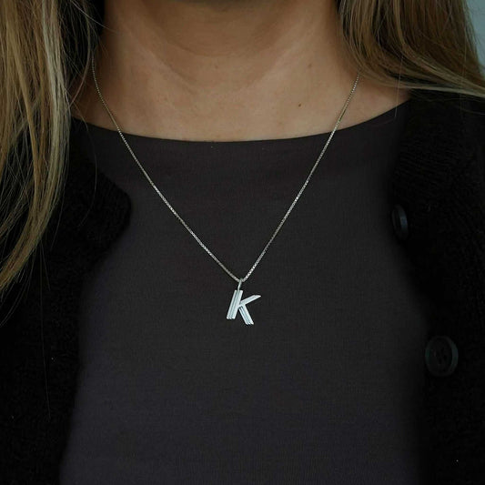 Silver necklace with a 'K' pendant worn by a person against a dark background