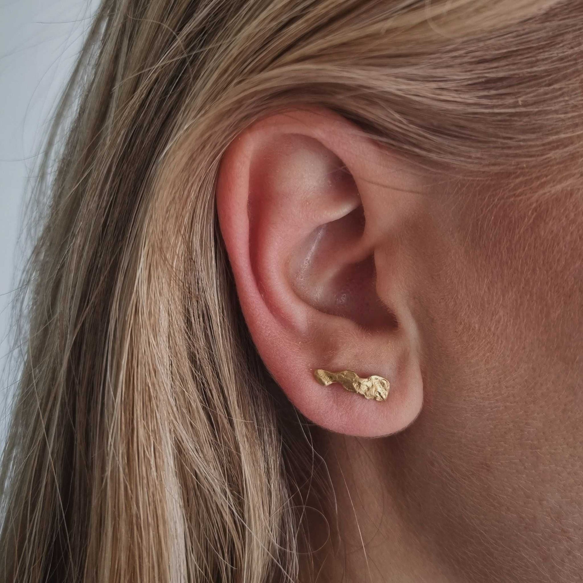 Close-up of an ear wearing a gold earring with blonde hair.