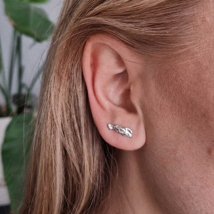 Close-up of an ear wearing a silver earring with blonde hair.