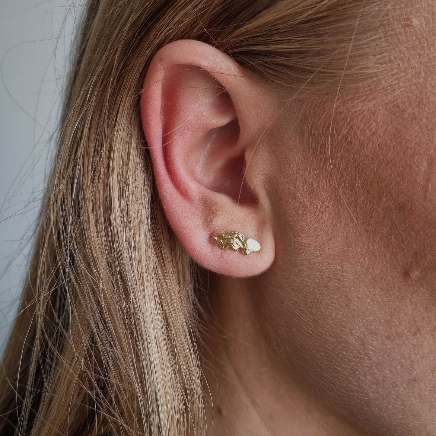 Close-up of an ear wearing a gold earring with blonde hair.