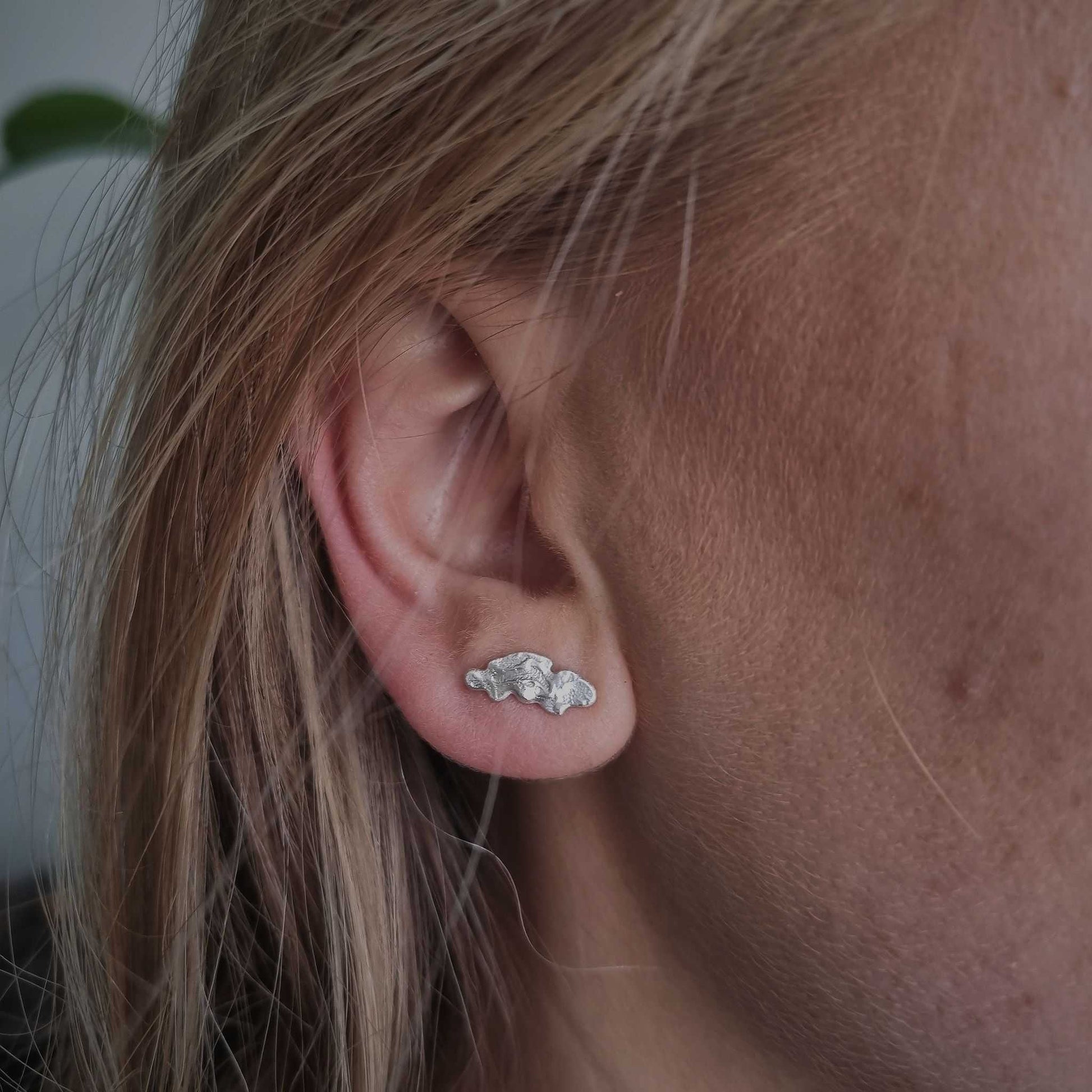 Close-up of an ear wearing a silver earring with blonde hair.
