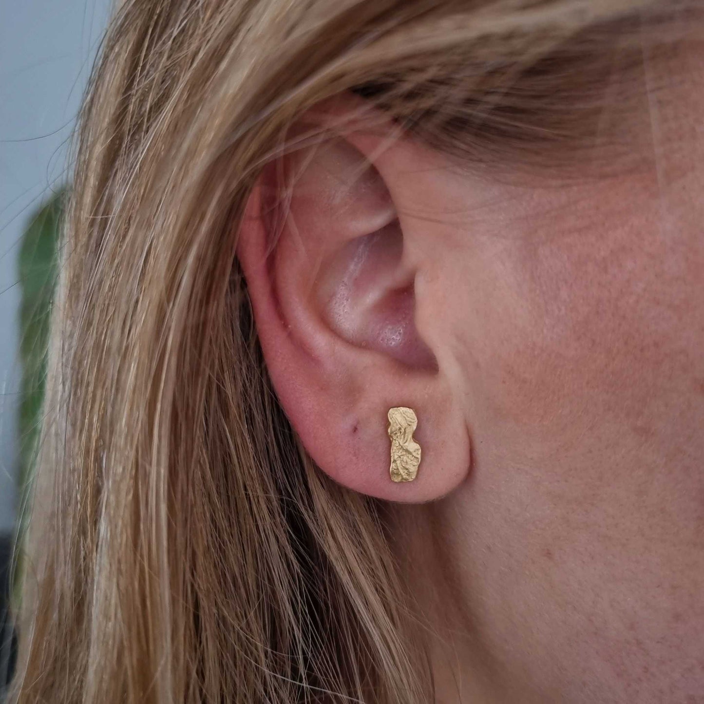 Close-up of an ear wearing a gold earring with blonde hair.
