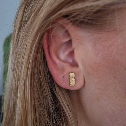 Close-up of an ear wearing a gold earring with blonde hair.