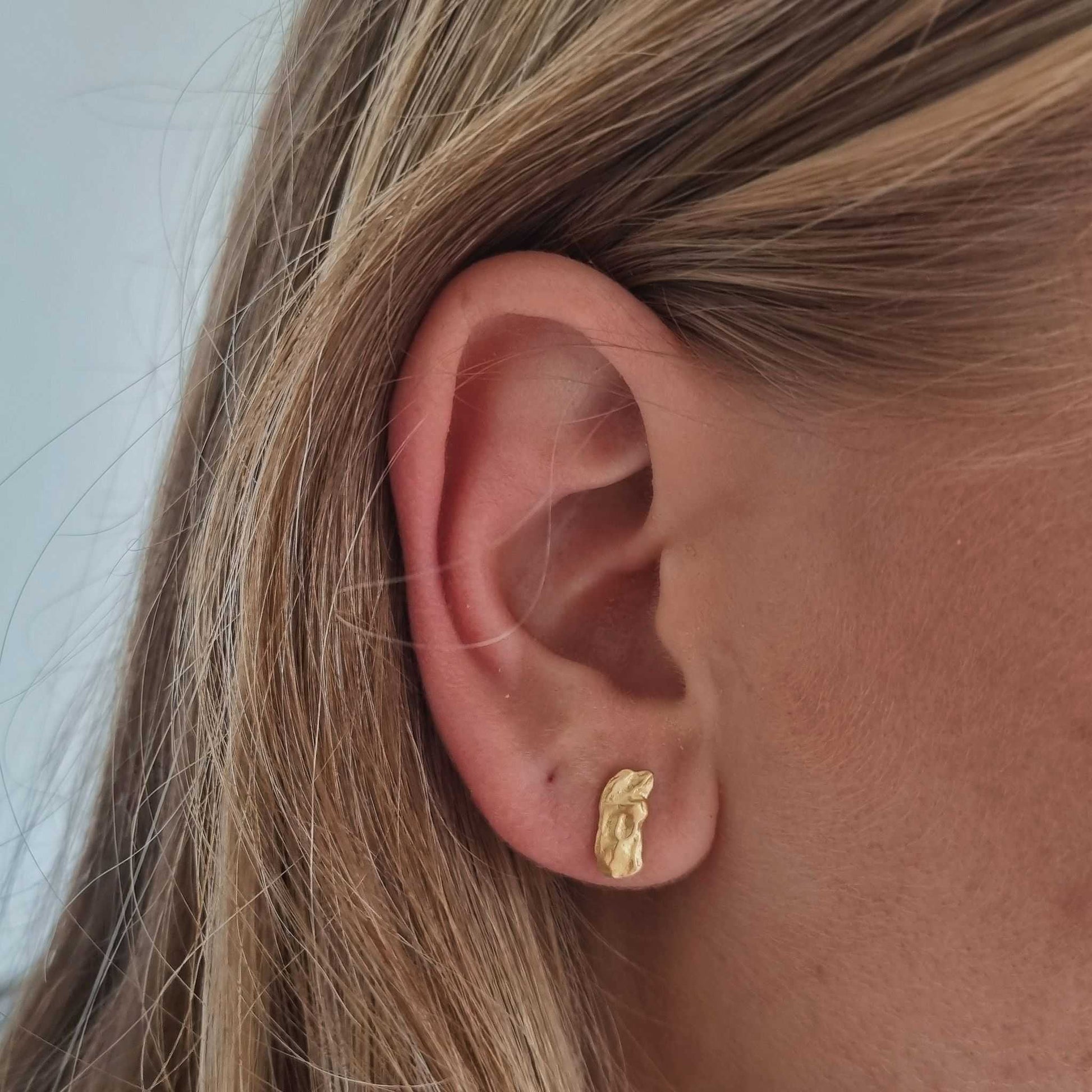 Close-up of an ear wearing a gold earring with blonde hair.