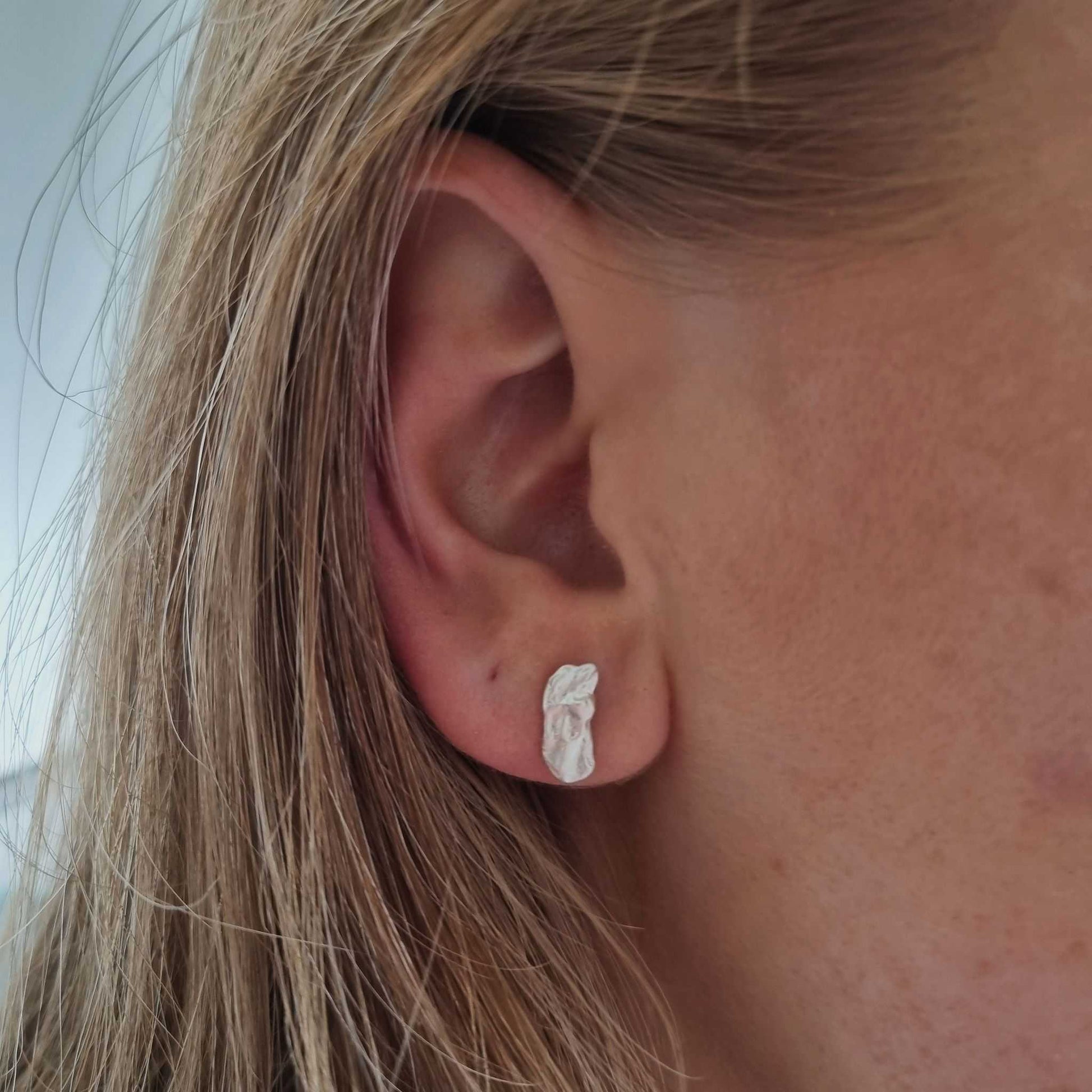 Close-up of an ear wearing a silver earring with blonde hair.