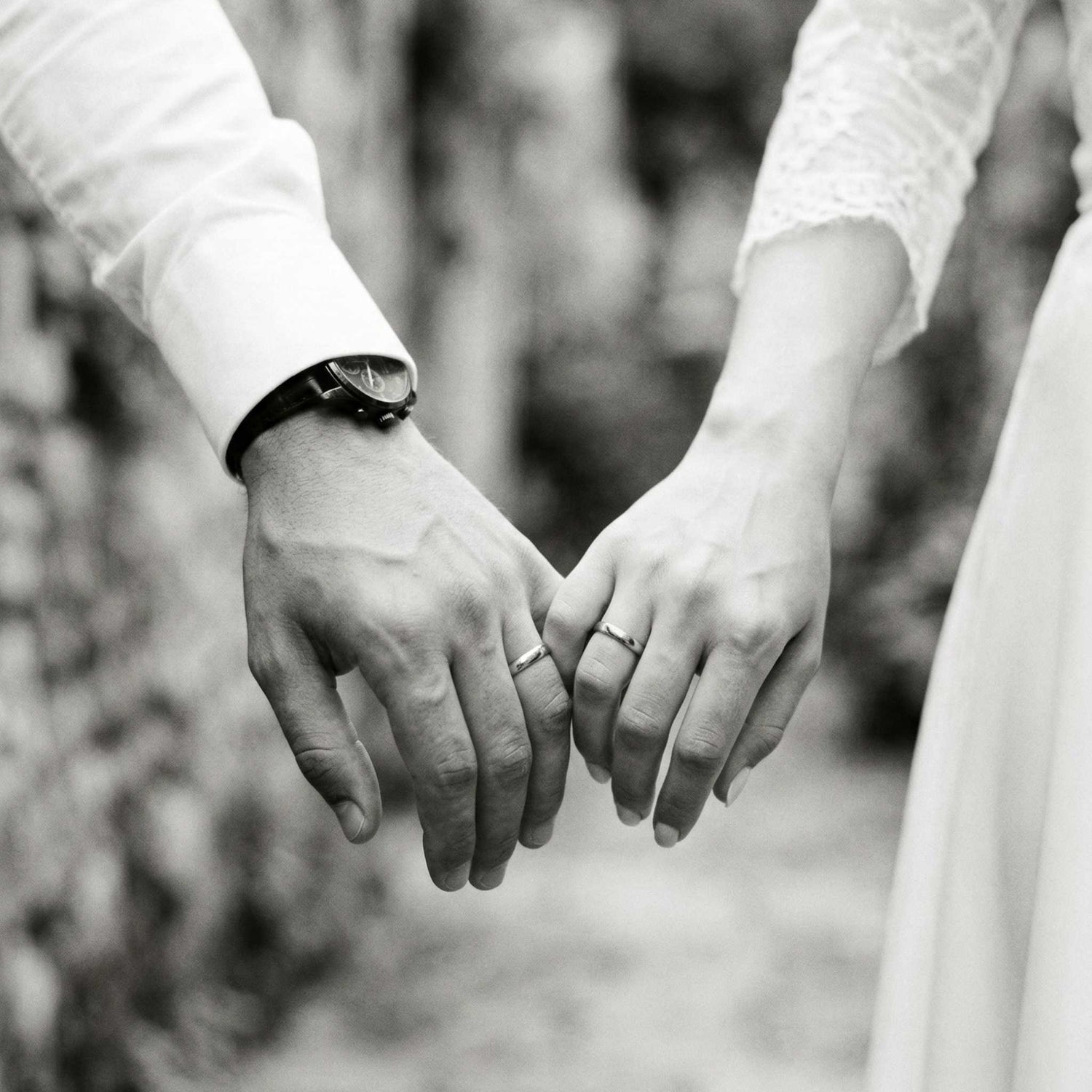 Two people holding hands wearing wedding rings with a blurred natural background
